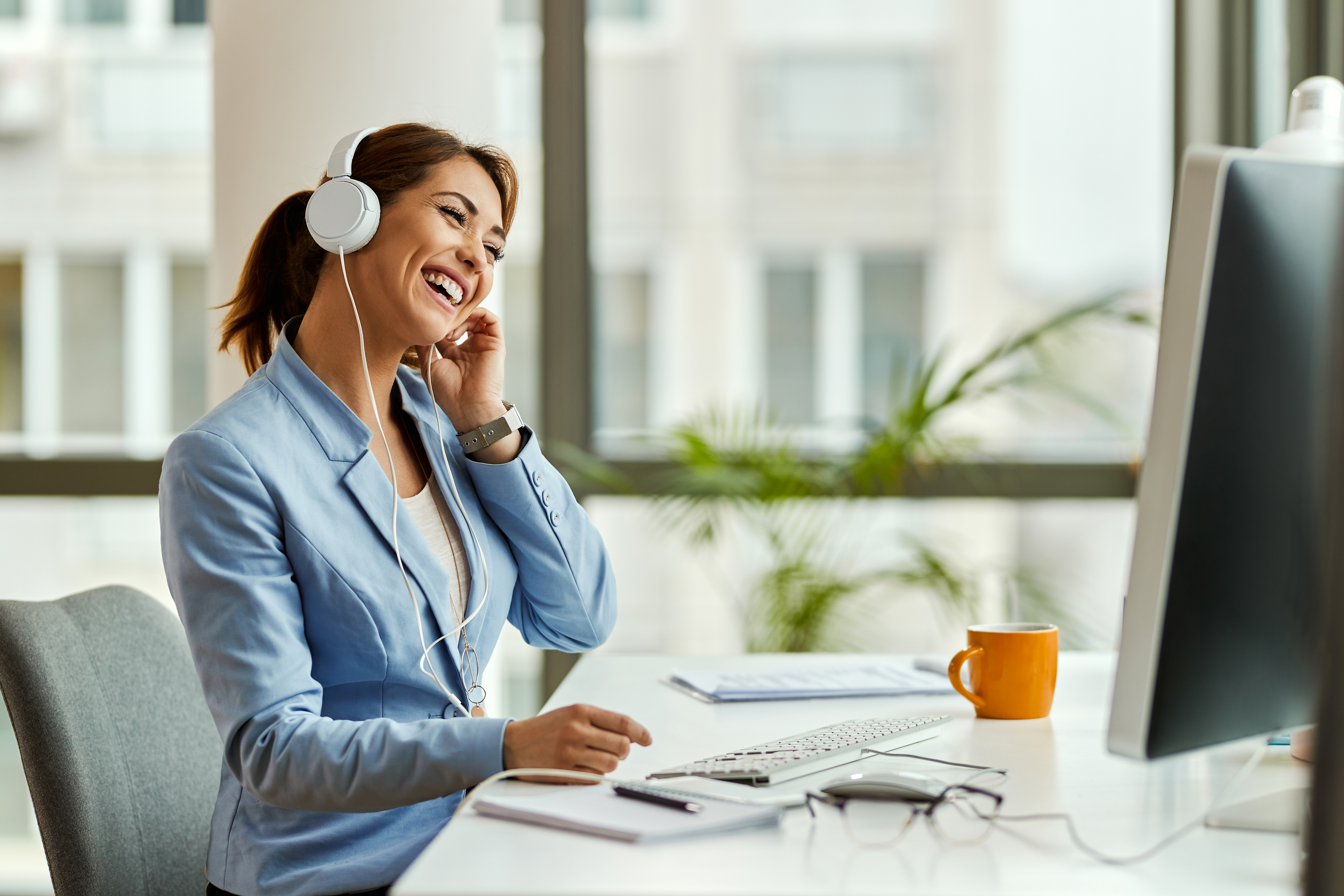 Young businesswoman having fun listening to music with headphones while working on computer in office